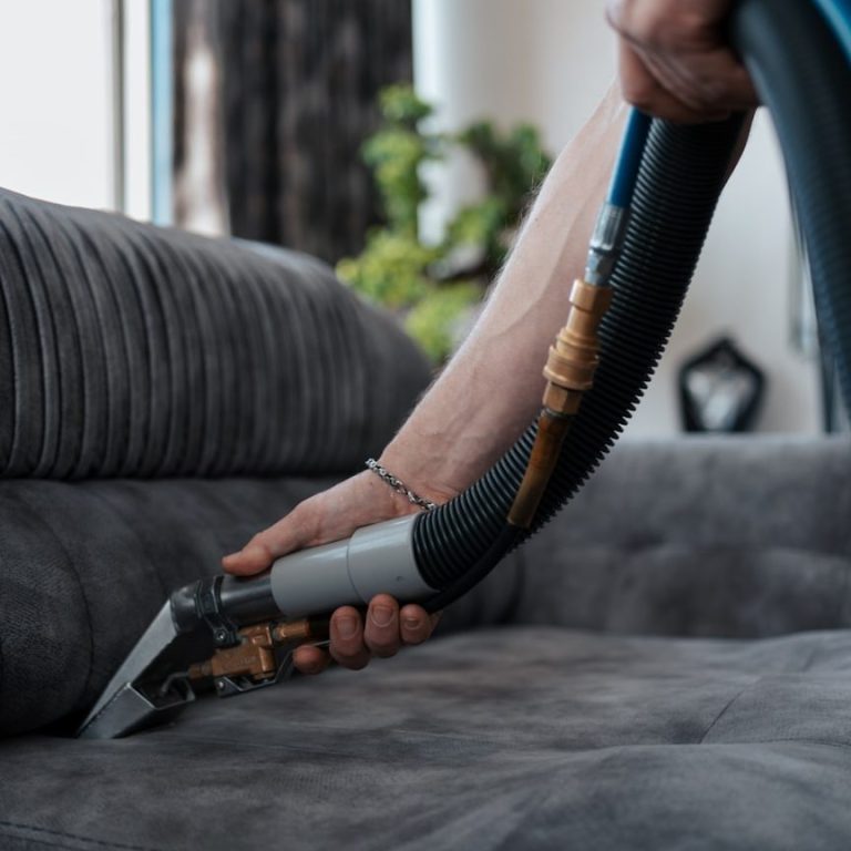 Jemand reinigt ein graues Sofa mit einem Teppichreiniger.