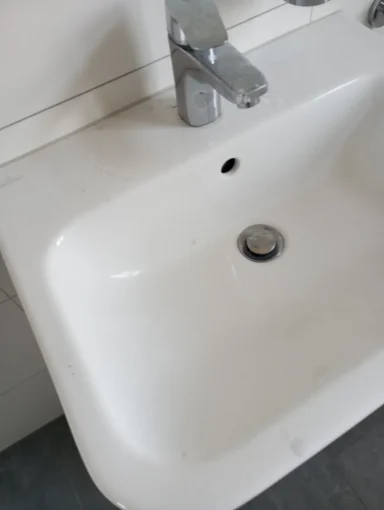 Weißes Waschbecken mit glänzendem Wasserhahn und Abfluss.