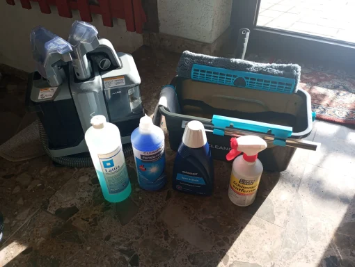 Reinigungsmittel und Putzutensilien auf einem Boden vor einem Fenster.